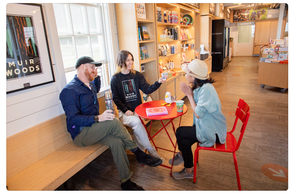 A group of friends sits and smiles over coffee at a table in the Warming Hut of San Francisco